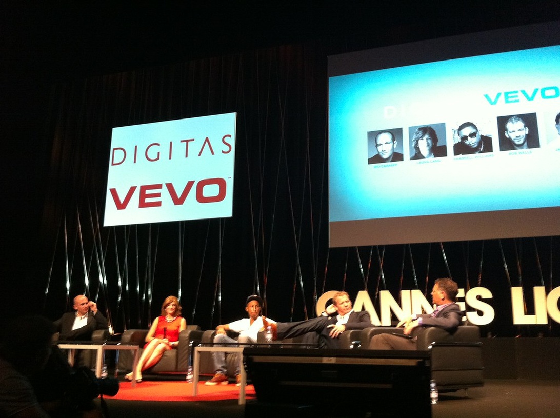 A panel discussion related to music video platform VEVO. Several people are seated on a stage with presentation screens behind them displaying the VEVO logo. This appears to be a music industry conference or event where industry professionals are discussing digital music distribution.